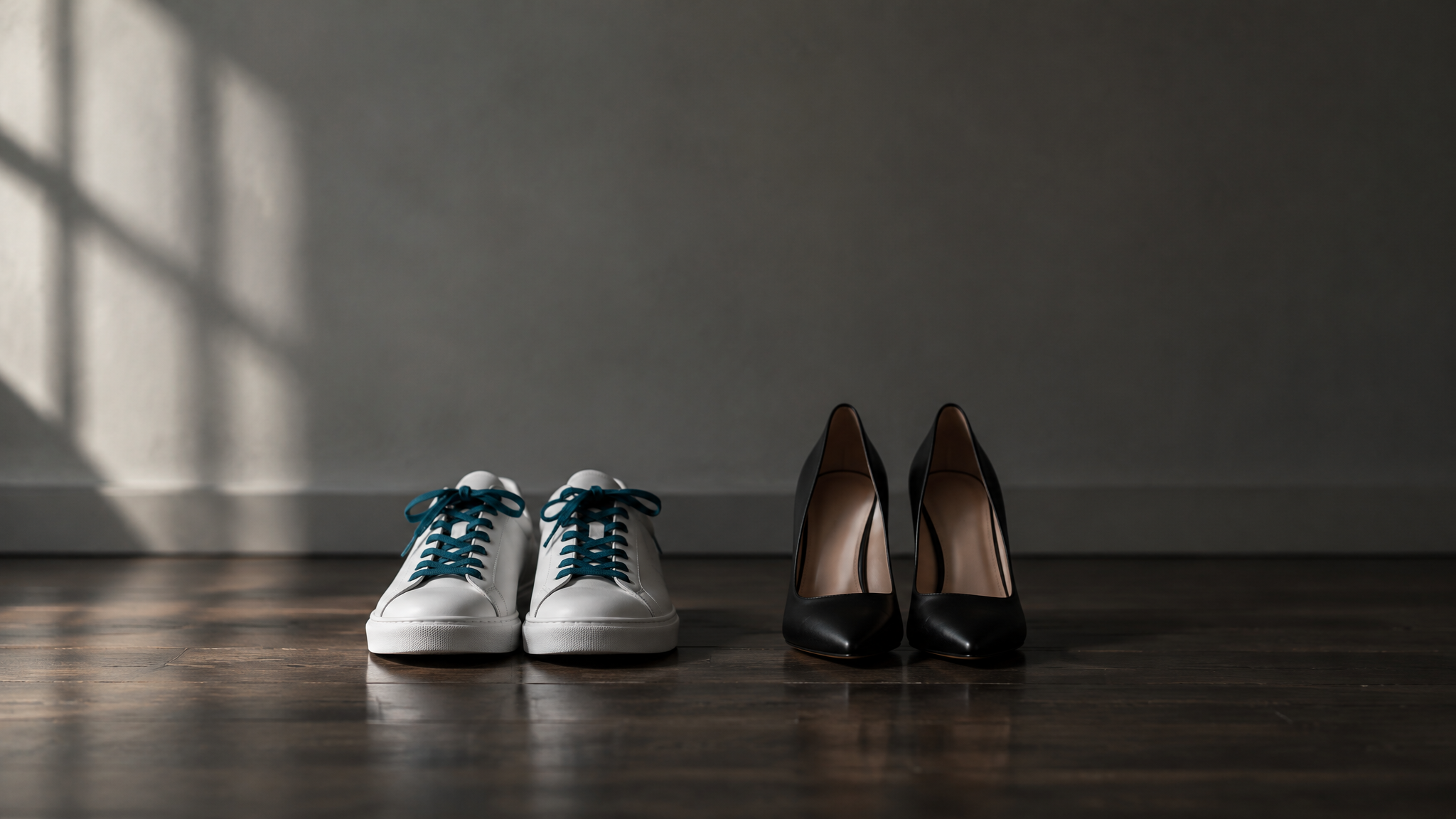 Weiße Turnschuhe und schwarze Pumps nebeneinander auf einem Holzboden im Licht eines Fensters