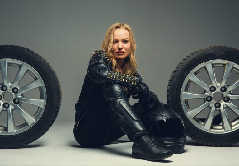 Female with motorcycle helmet sitting between two car wheels.